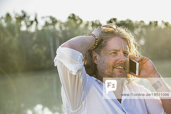 Man talking on mobile phone at riverbank  Bavaria  Germany