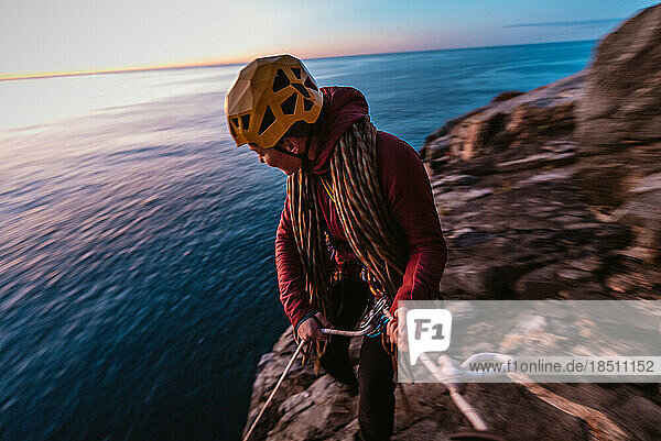 Woman rock climber getting ready to rappel on seaside cliff