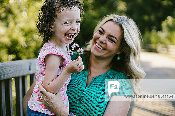 Mom hold and laughs with daughter who has picked flower