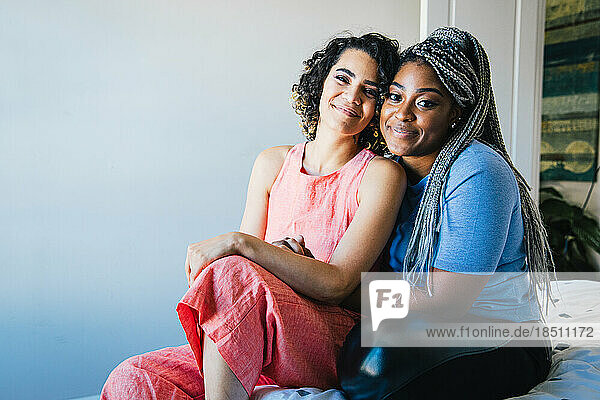 Portrait of smiling lesbian couple sitting on bed at home