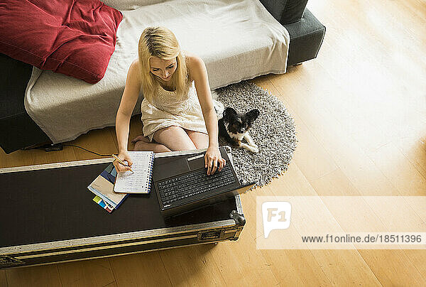 Beautiful young woman working on laptop with her dog in the living room  Munich  Bavaria  Germany