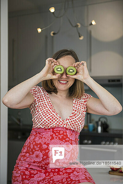 Pregnant woman having fun with pieces of kiwi in the kitchen and smiling  Munich  Bavaria  Germany