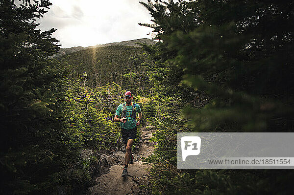 Man running through green forest on path with mountains
