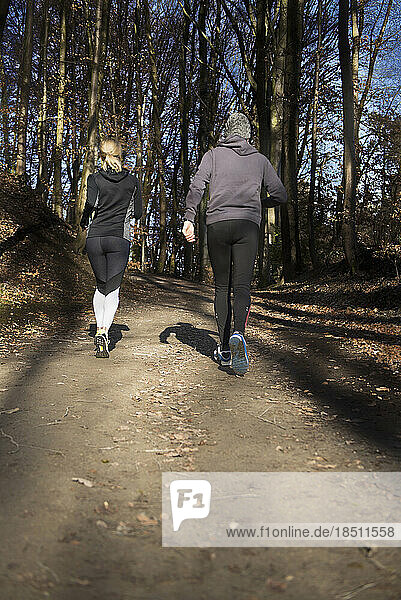 Rear view of man and woman in sportswear jogging on forest path