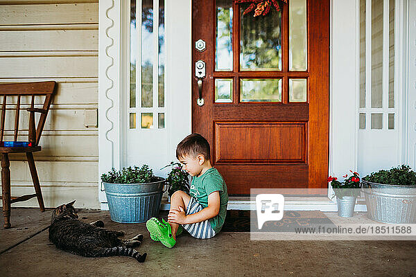 Young boy looking at pet cat on front porch in summer time