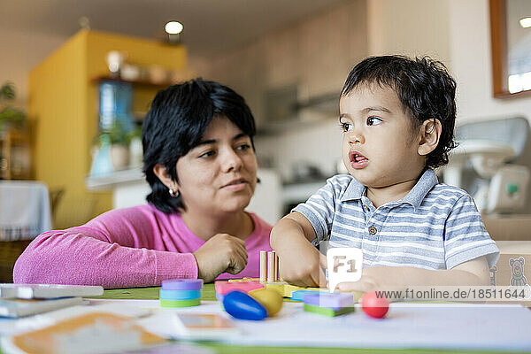 Latin mother and little son playing together with wooden logic toys.