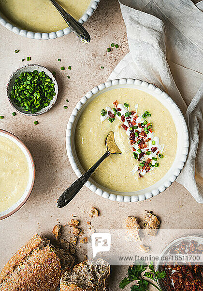 Bowls of potato leek soup and bread on beige background from above.