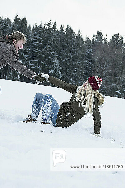 Young man helping his friend to stand up in snowy landscape  Bavaria  Germany