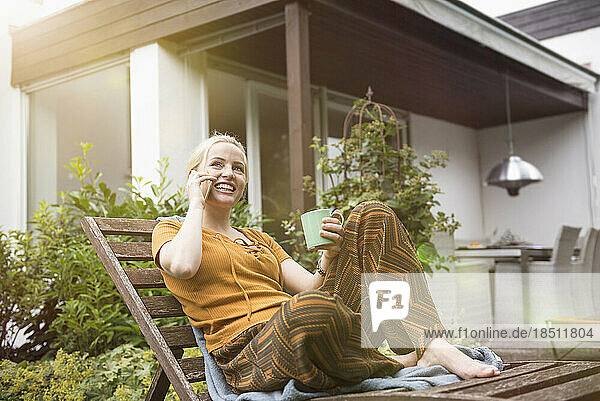 Beautiful young woman having cup of tea and talking on smartphone in the domestic garden  Munich  Bavaria  Germany