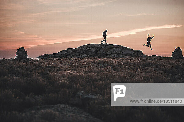 Silhouette male trail runners running over ridge at dawn sunrise