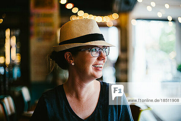 Woman in hat and glasses smiles in restaurant with bokeh light
