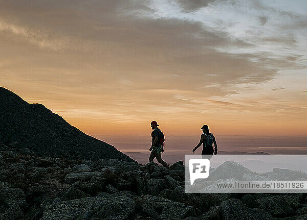 Two hikers walk along the top of Katahdin at dawn.