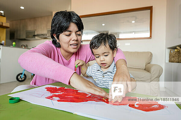 Latin mother and little son painting together hand using tempera