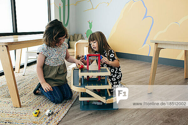 Two girls sit on the floor and play together with a car ramp toy