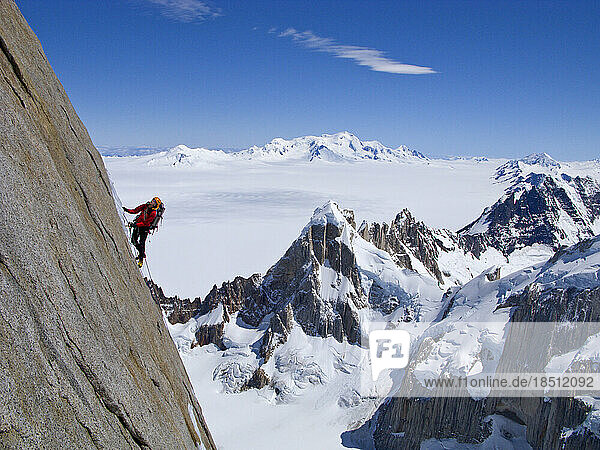 A climber climbs the steep north face of Torre Egger  with the peaks of Cerro Rincon below  and the glaciers of the Southern Pa