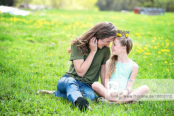 Mother and tween daughter sitting in a dandelion meadow.