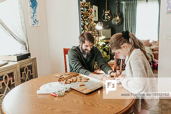 Father and daughter build gingerbread houses together at home