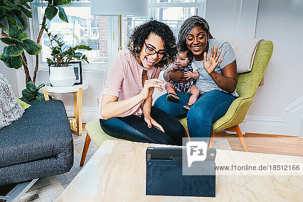 Smiling lesbians with baby enjoying video call on digital tablet at home