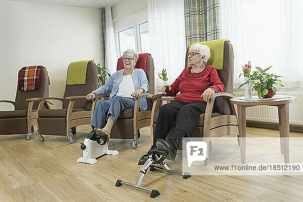 Two senior women doing exercise on mini foot pedal exerciser in rest home