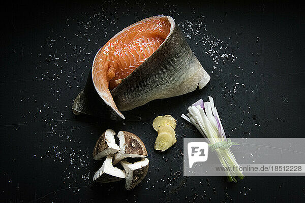 Raw salmon fillet with mushrooms  ginger  onion and salt on black tile