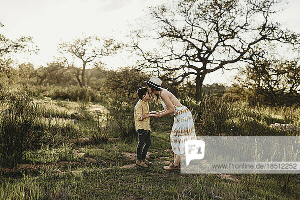Young mother bending down to kiss young son in backlit meadow