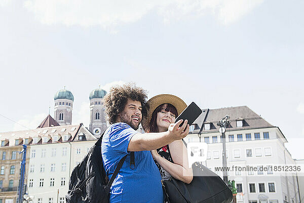 Couple taking selfie using mobile camera in front of Cathedral of Our Lady  Munich  Germany