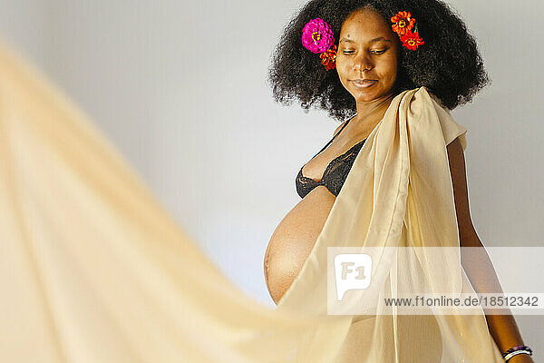 A pregnant woman with flowers in hair stands draped in gold fabric
