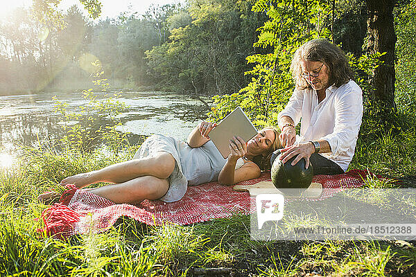 Couple on picnic using tablet with watermelon by river  Bavaria  Germany