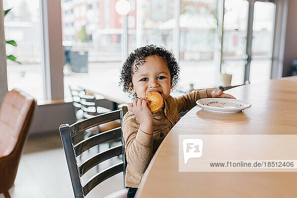 Adorable curly headed toddler eating a donut at cafe