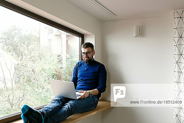 man in blue sweater and jeans is working alone at home with laptop