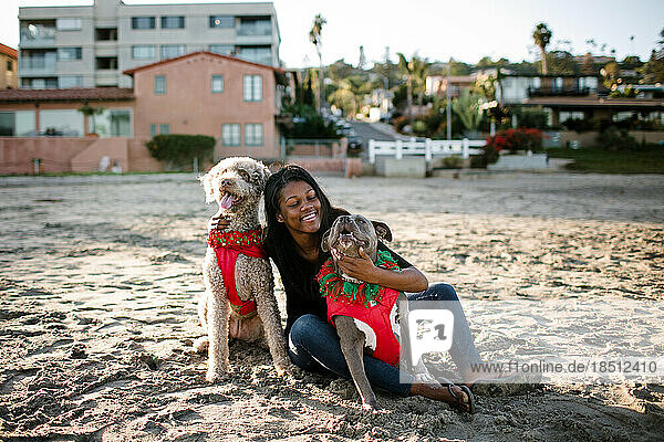 Young girl hugging and smiling at dogs on beach at sunset