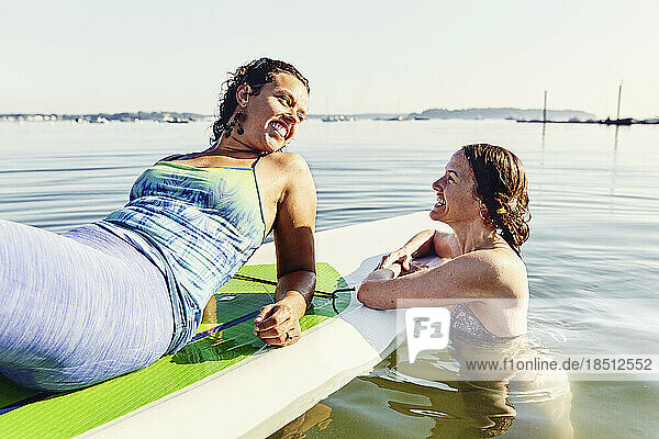 Two young female friends relax on standup paddle board in Casco Bay