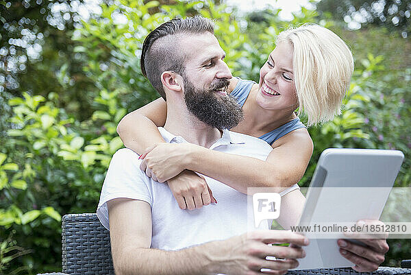 Young man using digital tablet with his girlfriend embracing from behind in garden  Bavaria  Germany