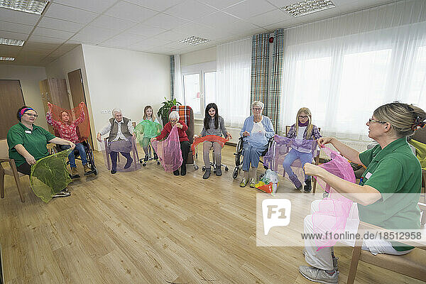 Girls with nurses and senior woman doing gentle sports exercise with cloth in rest home