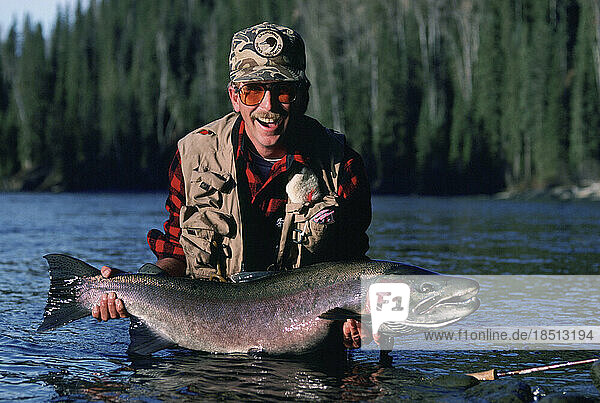 A smiling fly-fisherman holds a trophy steelhead trout in British Columbia.