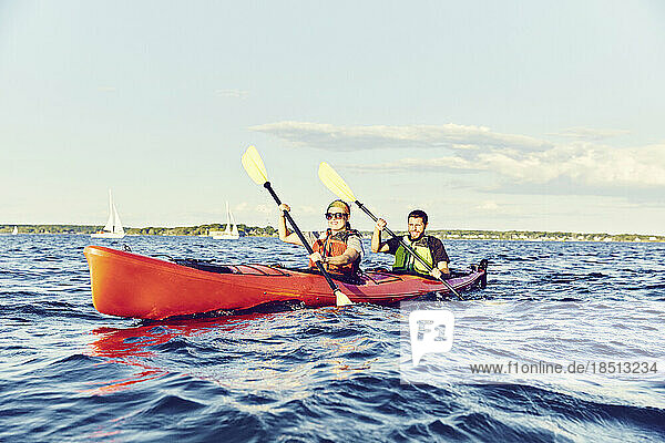 Young couple in tandem kayak paddle through Casco Bay at sunset