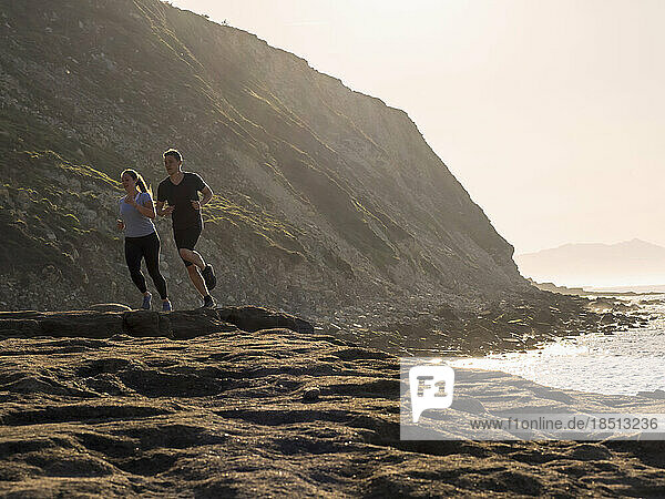 Man and woman running on single trail on coast at Azkorri beach