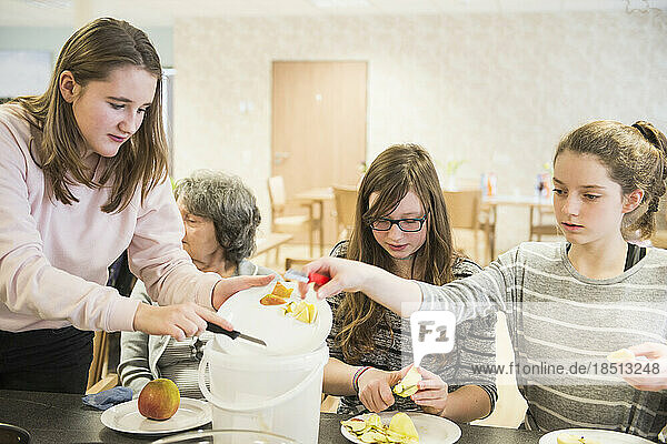 Senior woman with girls peeling apple at rest home