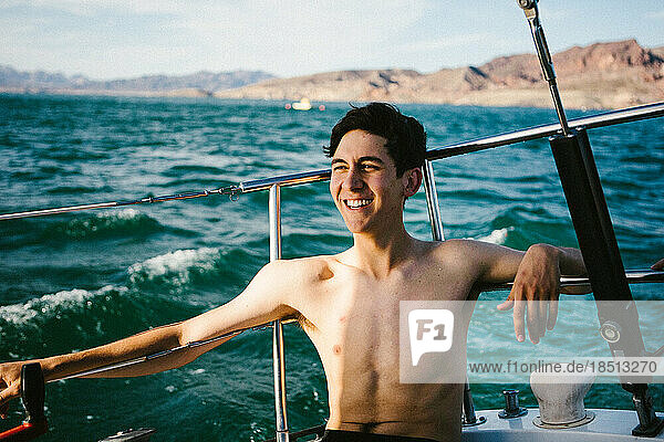 Young man smiles on sailboat on lake in summer sunshine