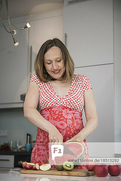 Pregnant woman cutting slices of watermelon in the kitchen  Munich  Bavaria  Germany