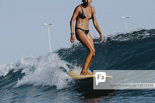 lower part of female surfer in bikini surfing on yellow longboard