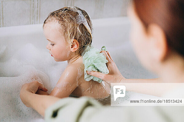 Woman bathes a little happy girl  Soaps her with a washcloth