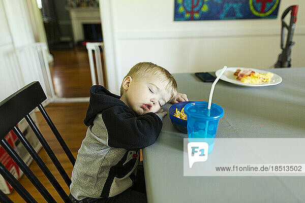 Toddler boy asleep in chair at dining room table during mealtime