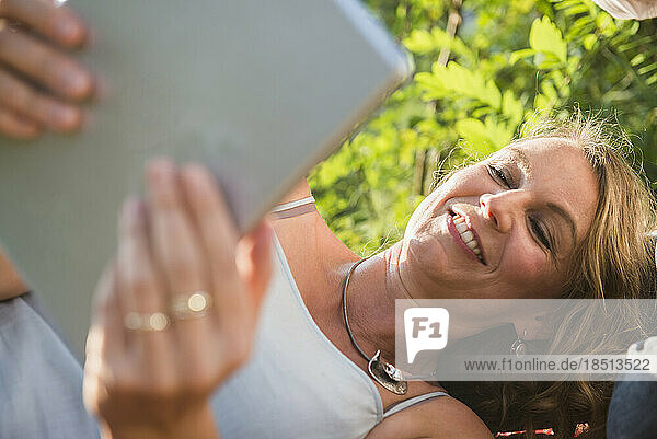 Happy woman lying on meadow using digital tablet