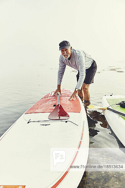 Mature man pushes his standup paddle board onto shore in the fog