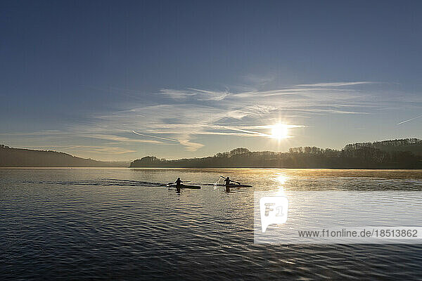 Silhouette of canoeists paddling in lake at sunrise