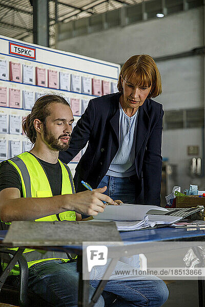Mature manager with worker looking at documents in warehouse