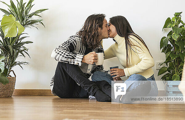 Romantic couple holding coffee cups kissing at new home
