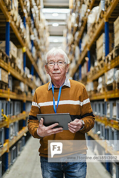 Confident senior man standing with tablet PC in warehouse