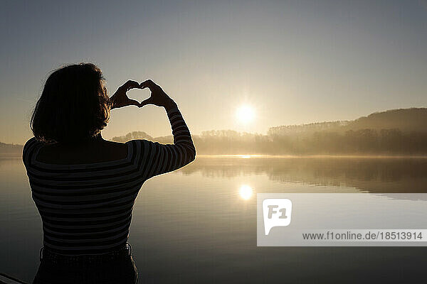 Frau macht eine herzförmige Geste vor dem See